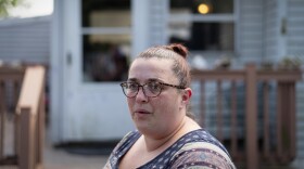 A woman with glasses and hair in a bun in front of a house 