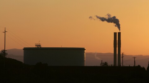 A picture of a refinery taken at dusk will hill in the background.