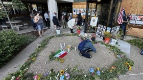 Candles, flowers and photos outside building. 