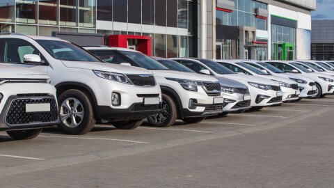  A row of new, white and grey cars line the lot at a dealership. 