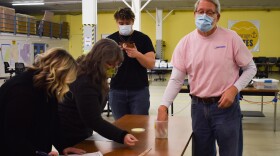 A man reaches into a jar while two women record at a table.
