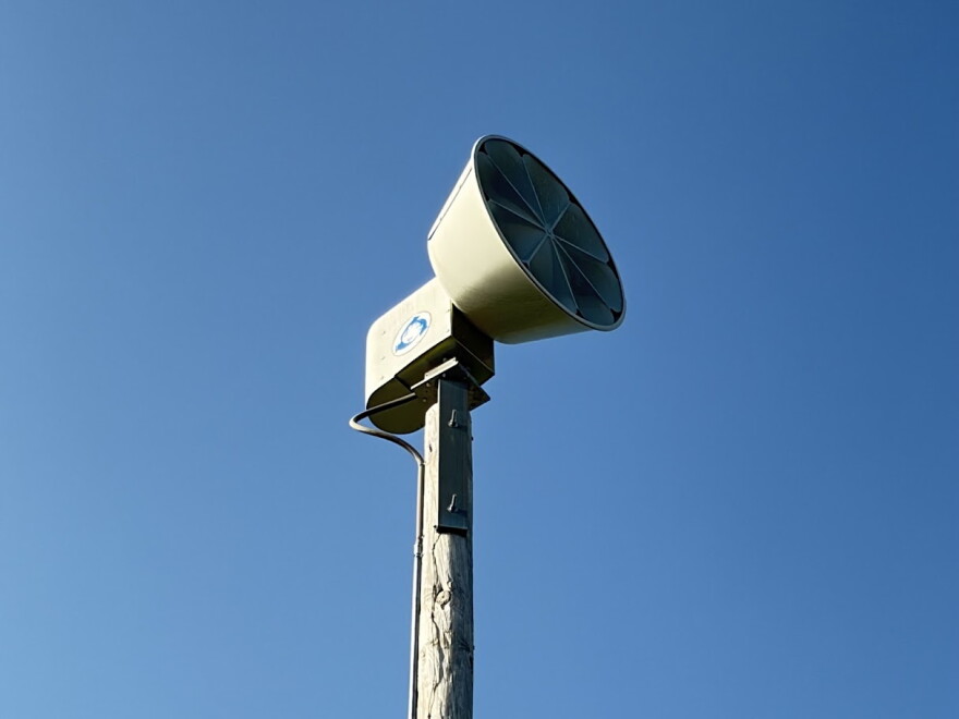 a siren on top of a light pole with blue sky behind it