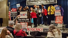 men and women stage next to several politically motivated signs. 