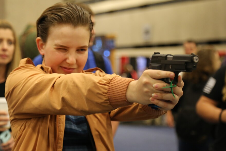 A high school student has both arms poised in front of her, aiming a gun. 