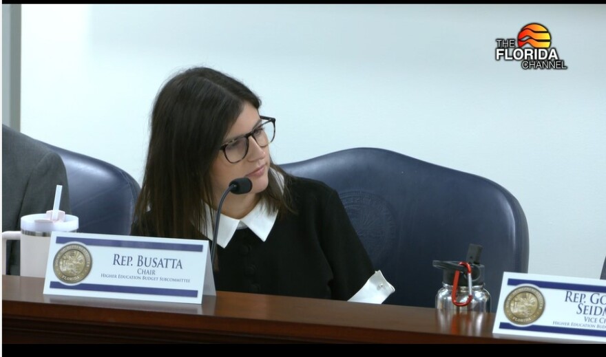 A woman in glasses and a white and black top sits in a House committee meeting