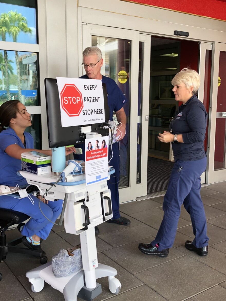 Nurse in scrubs seated at a table outside hospital door checking in patients