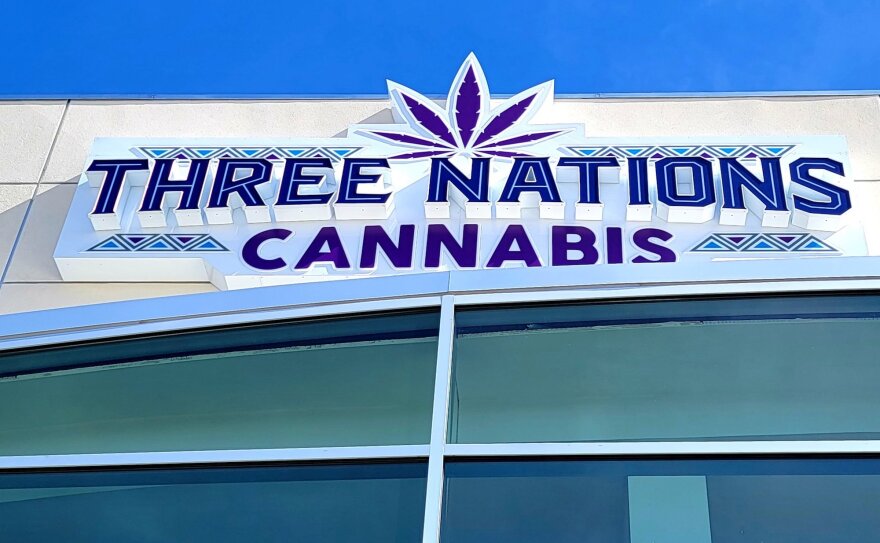 This is an image of a storefront sign that reads "Three Nations Cannabis" in dark purple letters. A purple marijuana logo is at the top of the sign. 