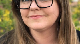 Woman with long brown hair and glasses looking into the camera