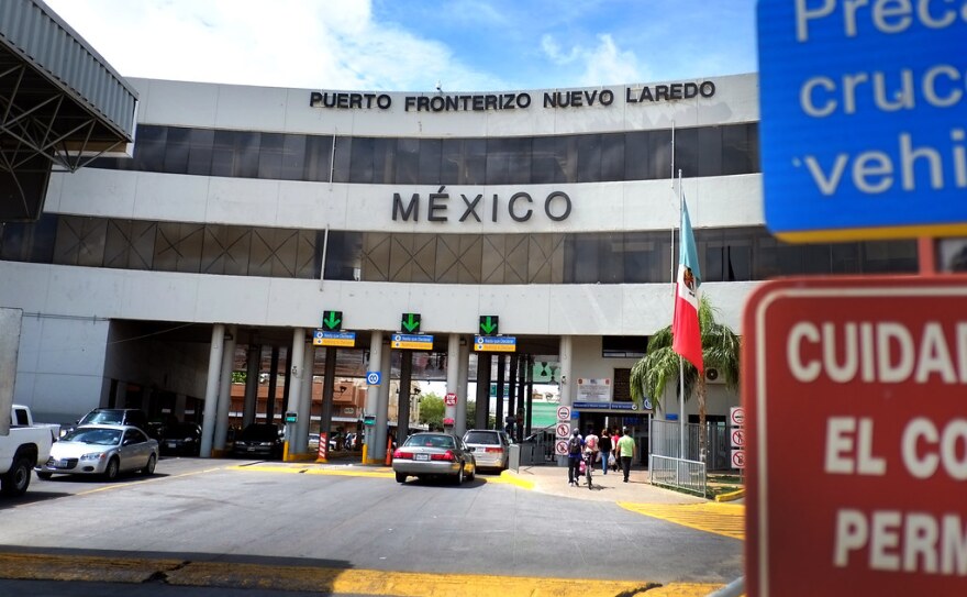 a three story building with tunnels underneath at the border to Mexico with cars driving under and a sign that says mexico on the building