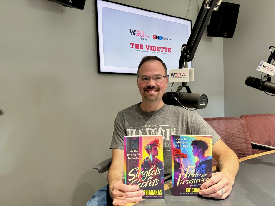 A man holds up two books with colorful covers while sitting, smiling, in a radio studio.
