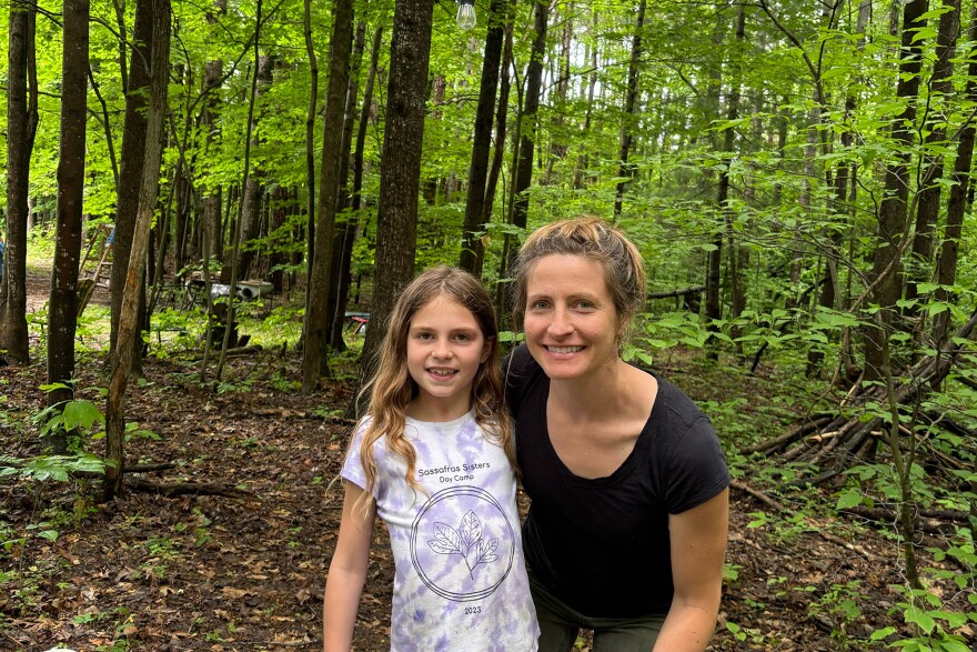 a girl and her mom smiling at the camera with green woods behind them