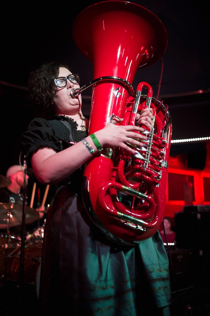 A woman in a green dress playing a red tuba