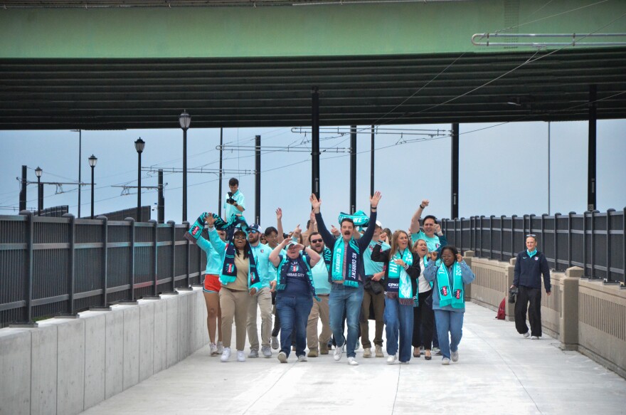 A group of people wearing teal clothing walk down a bridge.