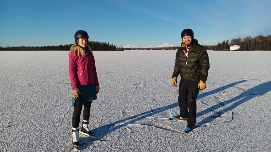 Two people skate on a snowy lake. 
