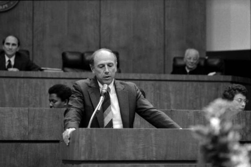 A man in a suit and tie at the Florida House podium, speaking into a microphone.jpg