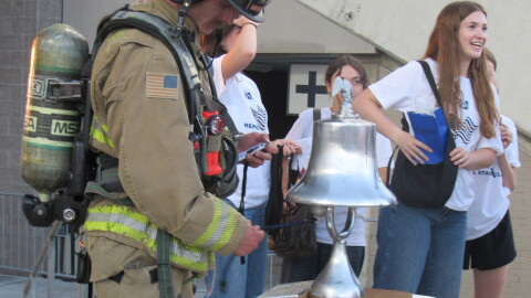 A man in a firefighter uniform rings a silver bell. 