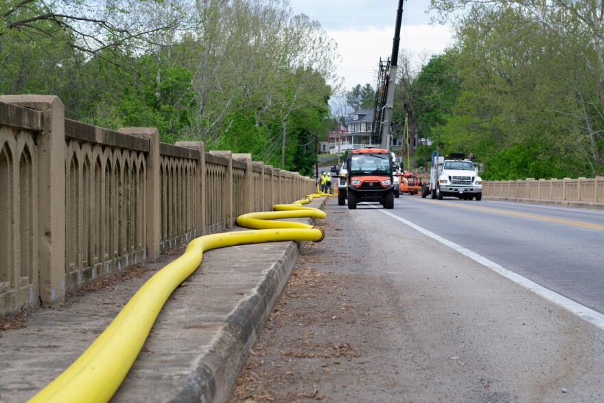A yellow fire hose carries water to the west end of Elkton while a public works crew replaces the broken sections of water line under the bridge.