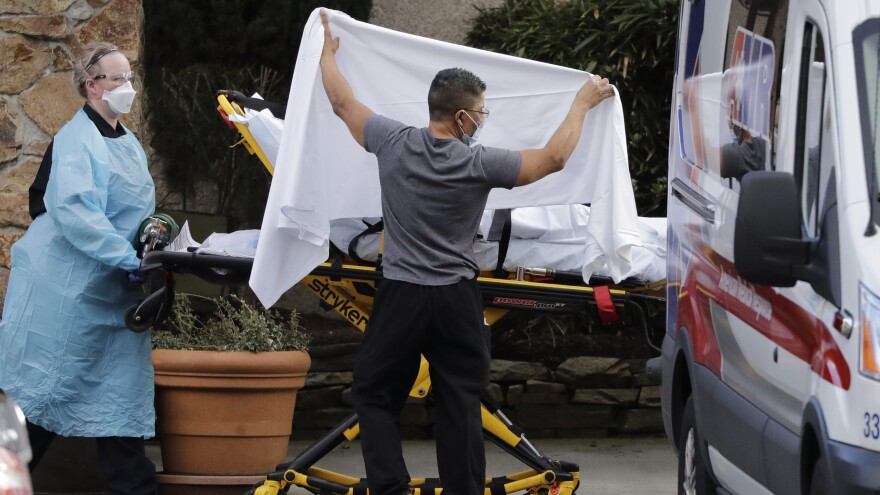 A staff member holds a sheet as a privacy screen as a person on a stretcher is taken to an ambulance from Life Care, a Kirkland, Wash., nursing facility where dozens of people are being tested for the COVID-19 virus.