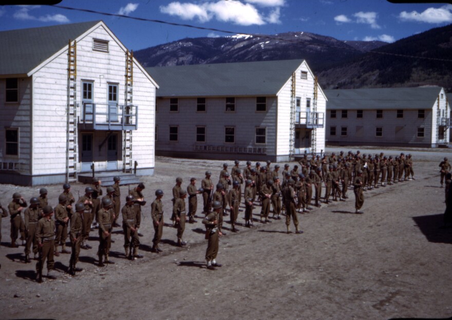 A group of several dozen soldiers in formation in front of three white buildings in the mountains near Leadville. Company F, 86th Mountain Infantry Regiment, in formation at Camp Hale. 1943-1944