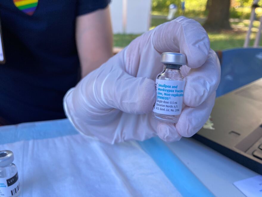 Dr. Sam Tochtrop holds a small, clear vial of the JYNNEOS monkeypox vaccine while wearing a latex glove. 