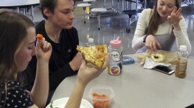 In this Friday, April 5, 2019 photo, Burlington High School student Emma McCobb, left, holds a piece of pizza while eating with classmates in the school cafeteria in Burlington, Vt.