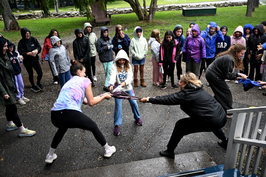 Alida Elliott-Bocassi 11, of Greenwich (center) jumps in to help her College League Dean Allie Berwick (left) and Caroline Degnan break free a tee shirt from the ice during the frozen tee shirt challenge at Experience Camps, a free grief camp for kids whose parent died, that expanded to Connecticut this year at Camp KenWood and KenMont, in Kent, Connecticut August 20th 2025.