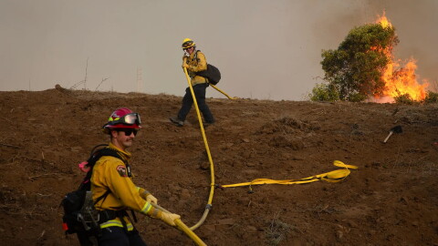 Cal Fire firefighters carry a fire hose up a hillside during the Sandy Fire in Simi Valley on May 18, 2026.