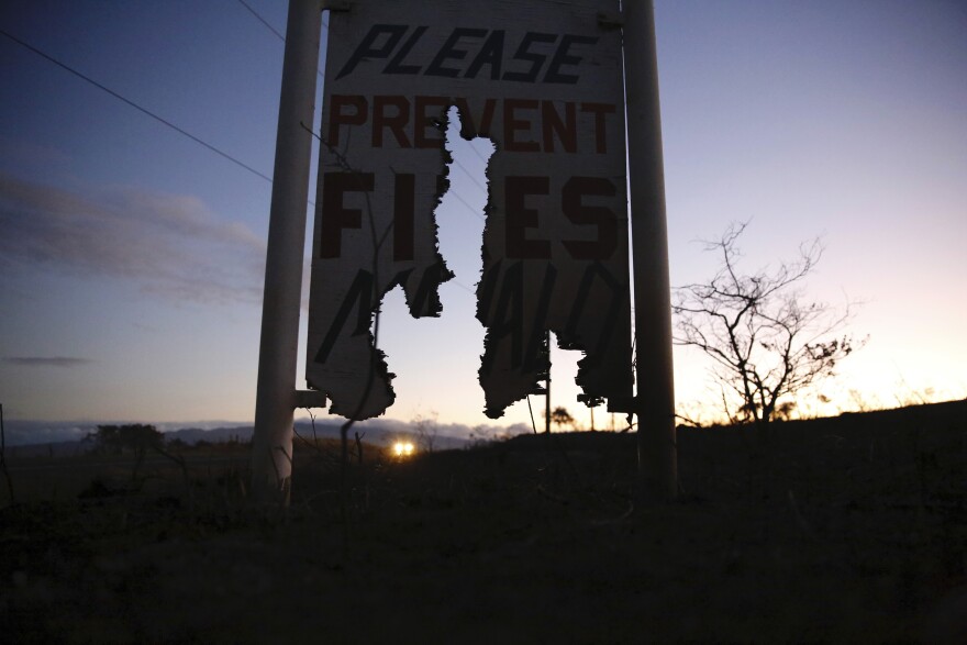 A car drives by a burnt roadside sign that says, "Please Prevent Fires, Mahalo," on Thursday, Aug. 5, 2021, in Waimea, Hawaiʻi. (AP Photo/Caleb Jones)