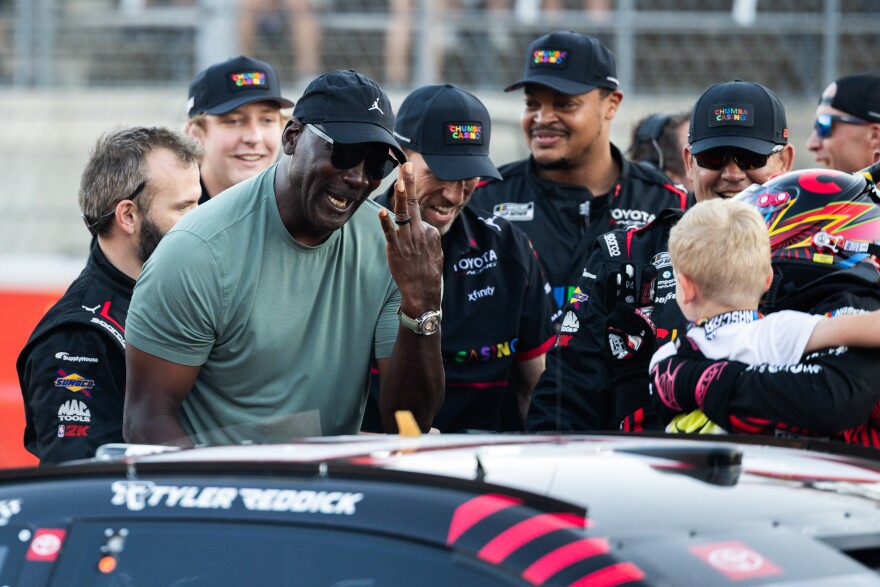 Michael Jordan, co-owner of the 23XI team, holds up three fingers as he celebrates with Tyler Reddick, who is holding his son, Beau. Reddick became the first driver in NASCAR history to open the Cup Series season with three consecutive wins.