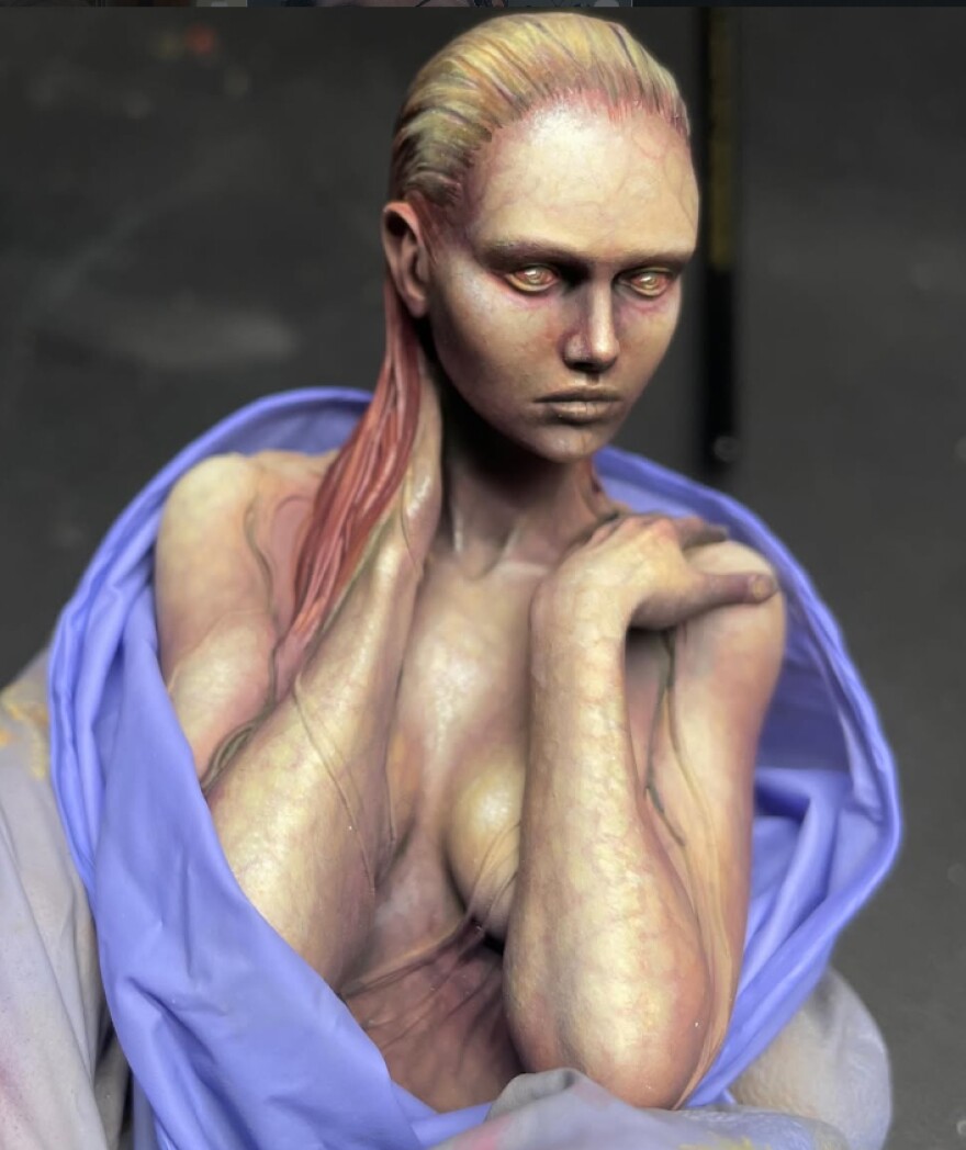 A mini figurine of a woman with her hands on her shoulders. The photo is a closeup of the figurine.