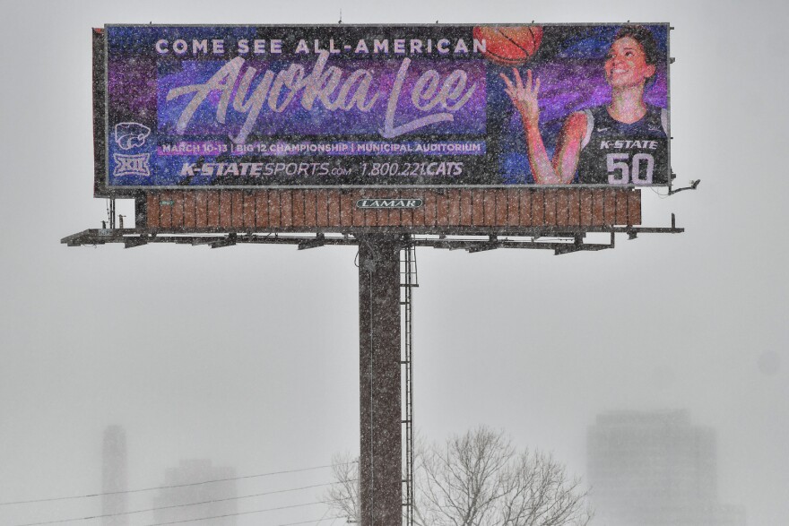 Billboard on a snowy day reads: "Come see All-American Ayoka Lee" and shows a female basketball player tossing a basketball. She wears a Kansas State jersey, number 50.