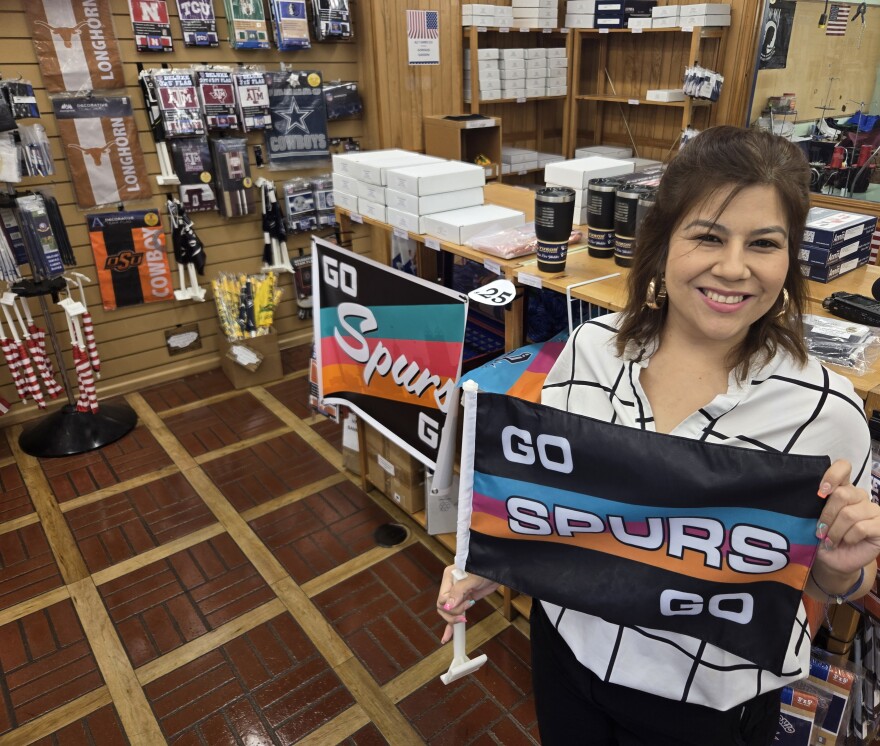Lorena Ortega, the sales and marketing manager at Dixie Flag & Banner Company, holds up one of their best sellers—a Spurs car flag