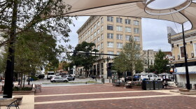 A brick- paved pedestrian square in downtown Athens with beige shade sails hovering above.