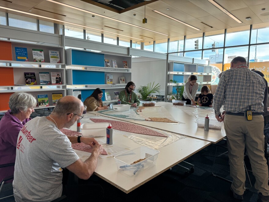 A group of people sitting around a table with arts materials and partially constructed mosaic pieces. 