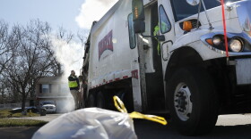 In this file photo, a sanitation worker rides the back of a truck as he works a residential route in Ohio.