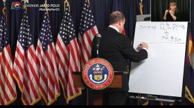 Gov. Jared Polis does math during a news conference to estimate how many vaccines the state will receive in the coming weeks.