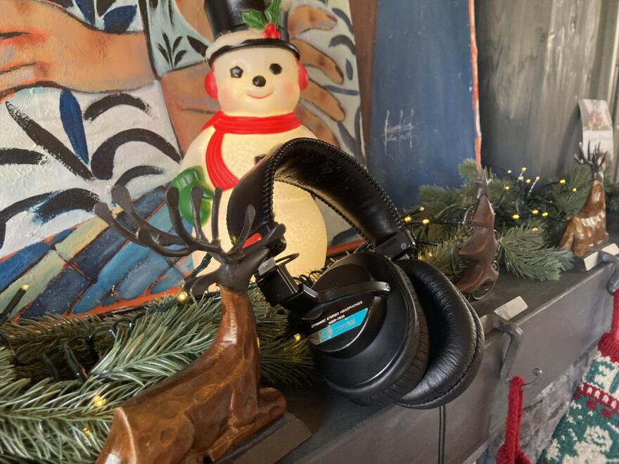 headphones rests on a holiday-decorated mantle with garland, wooden reindeer figurines, string lights, and a snowman decoration in the background.
