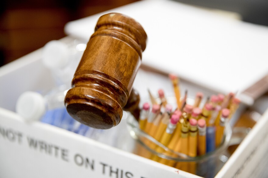 A wooden gavel pokes out of a bin, which also holds pencils and a water bottle