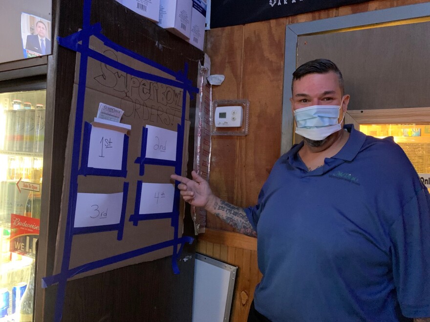 man wearing mask points at board with four lists