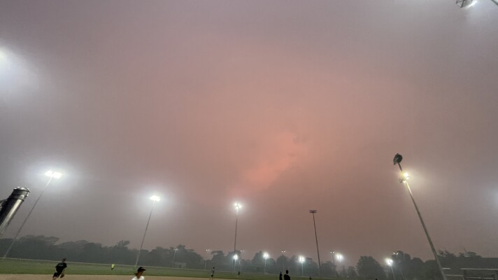 players on a softball field with a hazy, smoky, red sky above them