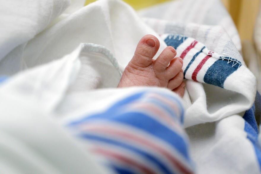 Wrinkly baby toes stick out from a white blanket with pink and blue stripes.