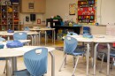 An empty classroom with round desks and blue plastic chairs around them