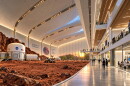 Rendering that shows the inside of a academic building with science labs on the right, a hallway with people walking in the middle and a simulated rocky planet surface with a rover, astronaut and small white building with a NASA sign on it.