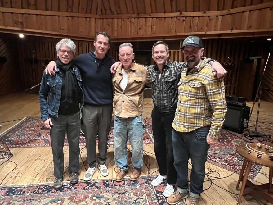 Five men stand in a music studio. 