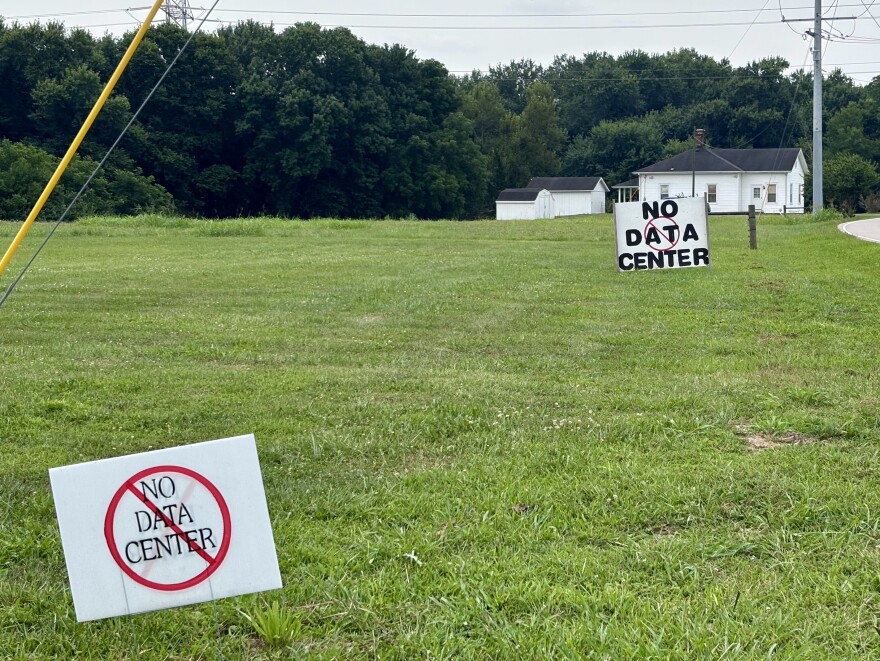 In a field of grass, two signs, one larger than the other, depict the words "No data center" with a prohibition symbol.