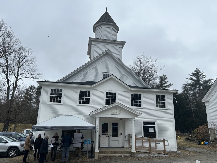 Several people stand outside of a white town hall building 