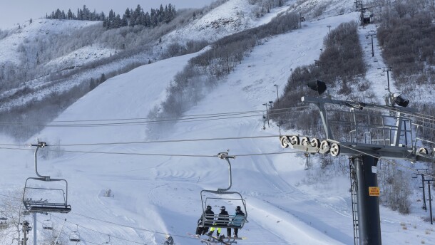 A chair lift on a mountain carries skiers up a massive hill covered in snow.