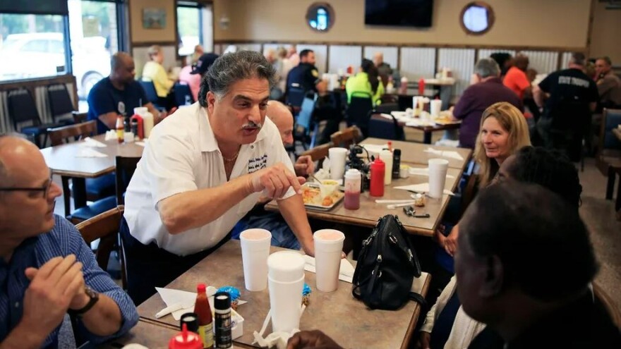 Owner Junior Kassees talks to Bishop Lorenzo Hall, bottom right, as Rick Alexander, left, listens Wednesday, April 19, 2023, at Junior’s Seafood Restaurant and Grill