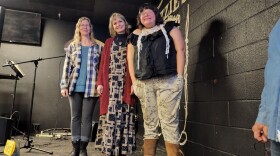 Three women stand on a stage at a poetry slam event