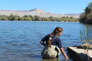 A woman sits at the edge of a large body of water.